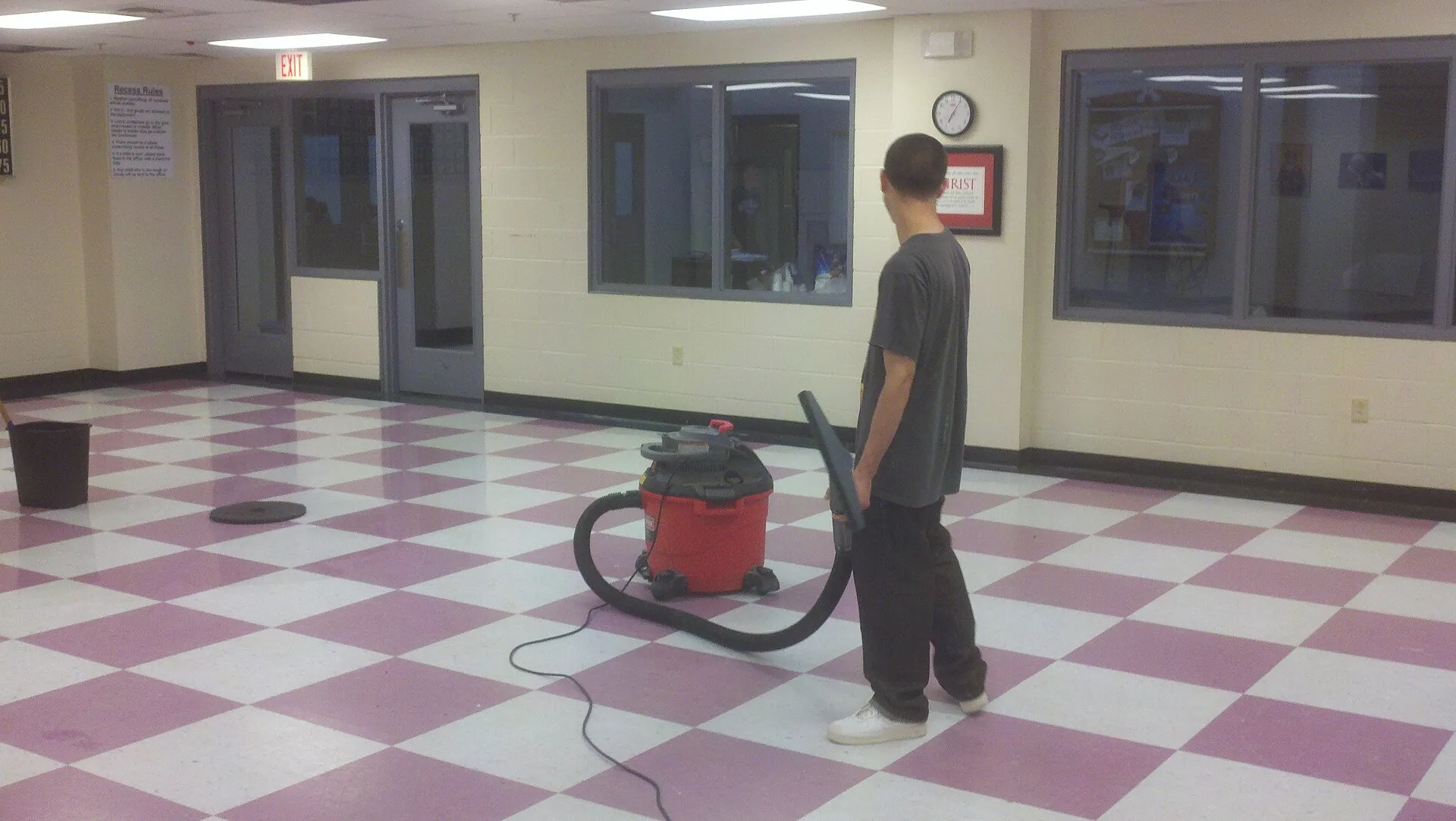 Janitorial worker vacuuming the floor of a commercial building corridor.